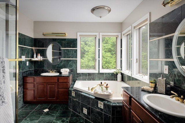 bathroom with tiled tub, vanity, and tile walls