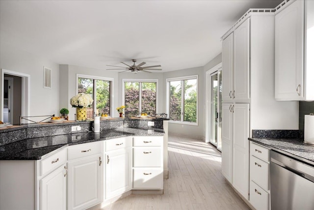 kitchen featuring white cabinets, plenty of natural light, dark stone counters, and dishwasher