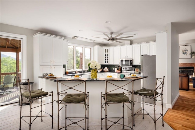 kitchen with white cabinetry, backsplash, kitchen peninsula, stainless steel appliances, and a healthy amount of sunlight