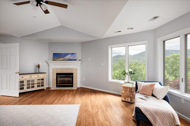 living room featuring ceiling fan, a fireplace, vaulted ceiling, and light wood-type flooring