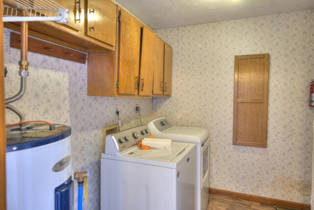 laundry area with cabinets, electric water heater, wood-type flooring, a textured ceiling, and separate washer and dryer