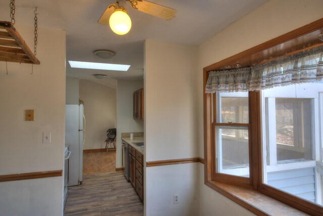 kitchen with hardwood / wood-style flooring, ceiling fan, a skylight, white refrigerator, and stainless steel dishwasher