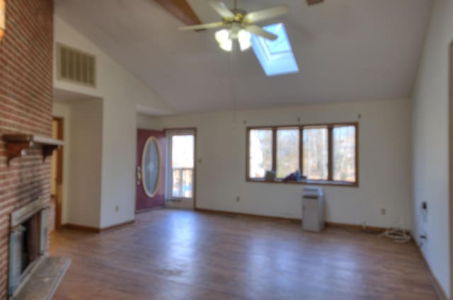 unfurnished living room with ceiling fan, hardwood / wood-style floors, a skylight, high vaulted ceiling, and a brick fireplace