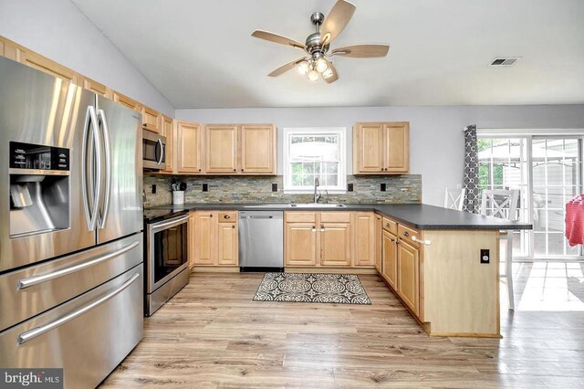 kitchen with decorative backsplash, dark countertops, appliances with stainless steel finishes, light brown cabinets, and a sink