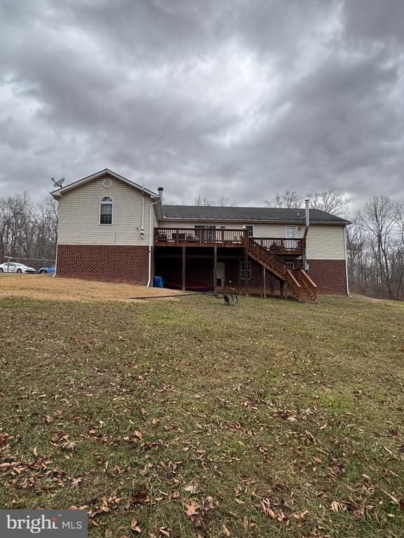 rear view of house with brick siding, stairs, a lawn, and a wooden deck