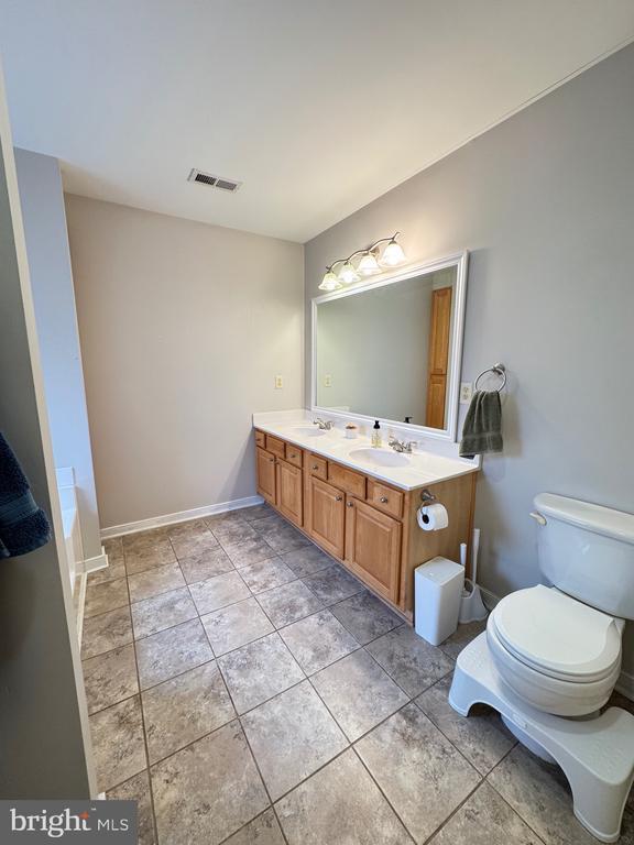 bathroom with toilet, a sink, visible vents, baseboards, and double vanity