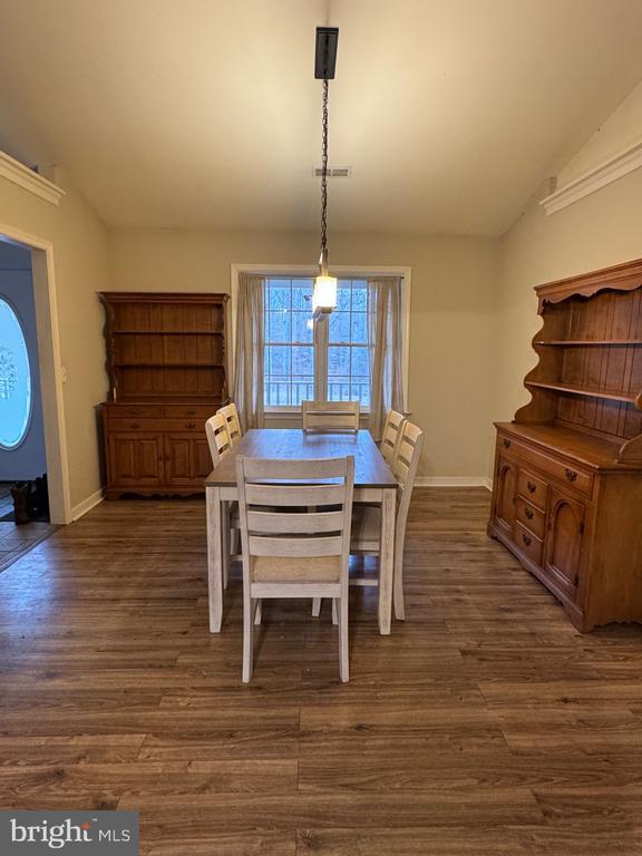 dining area featuring dark wood-style floors, visible vents, vaulted ceiling, and baseboards