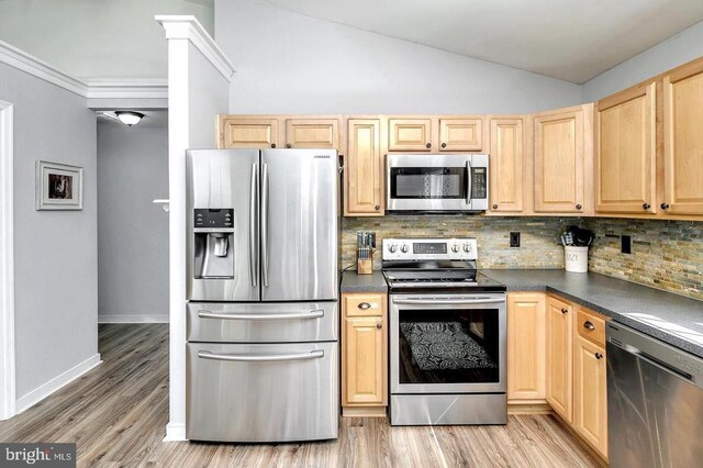 kitchen featuring lofted ceiling, stainless steel appliances, light wood finished floors, and dark countertops