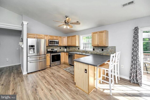 kitchen with stainless steel appliances, dark countertops, visible vents, light brown cabinets, and a peninsula