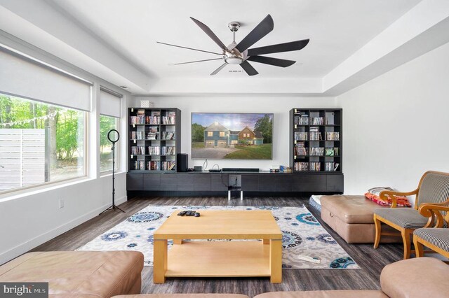 living room featuring a raised ceiling, dark wood-type flooring, and ceiling fan