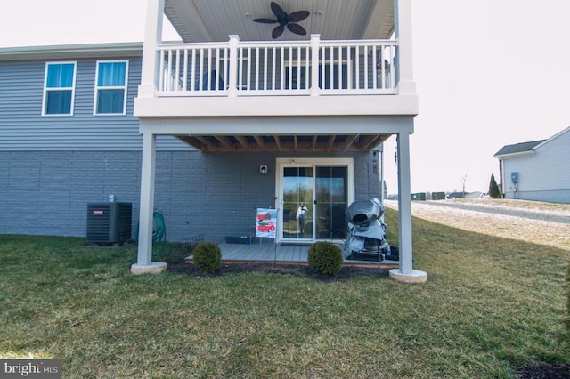 rear view of house with central AC unit, a balcony, brick siding, a ceiling fan, and a yard