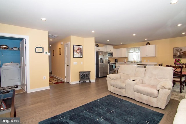 living room featuring recessed lighting, washer / dryer, wood finished floors, baseboards, and a wood stove