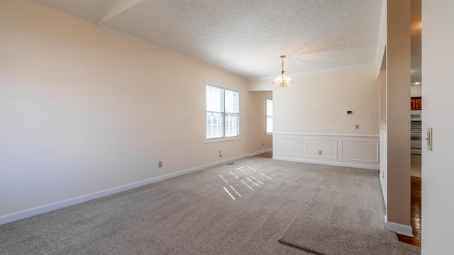 empty room with a textured ceiling, crown molding, carpet floors, baseboards, and an inviting chandelier