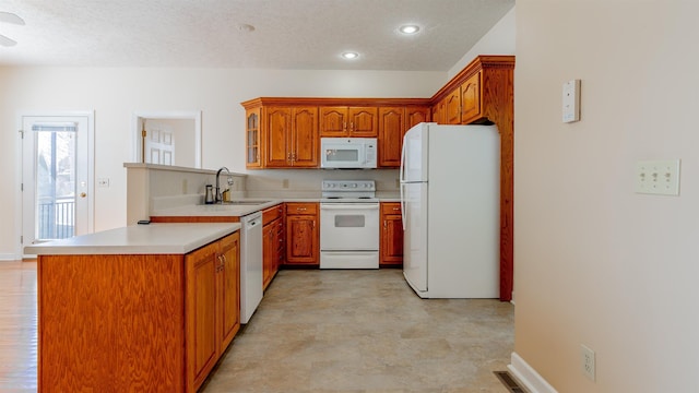 kitchen featuring white appliances, brown cabinets, a peninsula, light countertops, and a sink