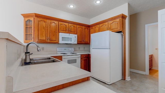 kitchen featuring white appliances, a sink, light countertops, brown cabinets, and glass insert cabinets