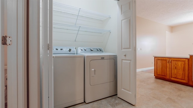 washroom featuring laundry area, baseboards, a textured ceiling, and washing machine and clothes dryer