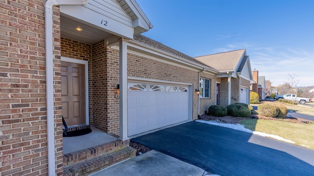 view of side of property with driveway, brick siding, an attached garage, and a shingled roof