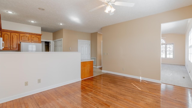 unfurnished living room featuring visible vents, baseboards, a textured ceiling, and light wood finished floors