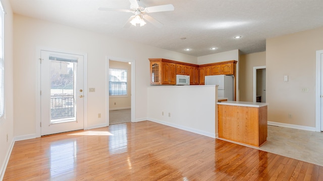 kitchen with white appliances, light wood finished floors, brown cabinets, a peninsula, and light countertops