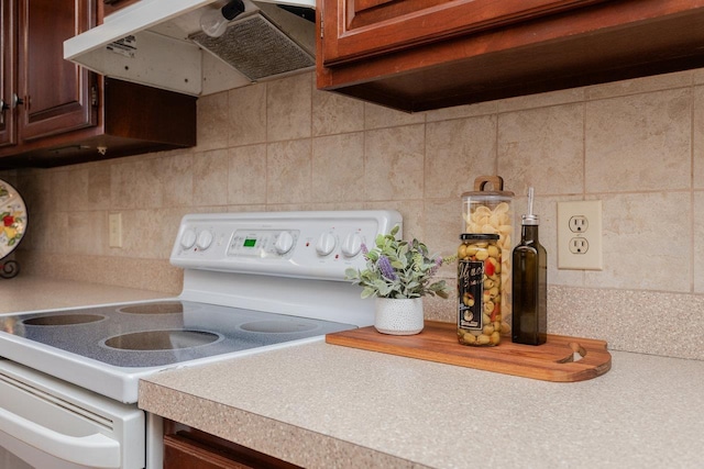 interior details with under cabinet range hood, white range with electric stovetop, light countertops, and backsplash