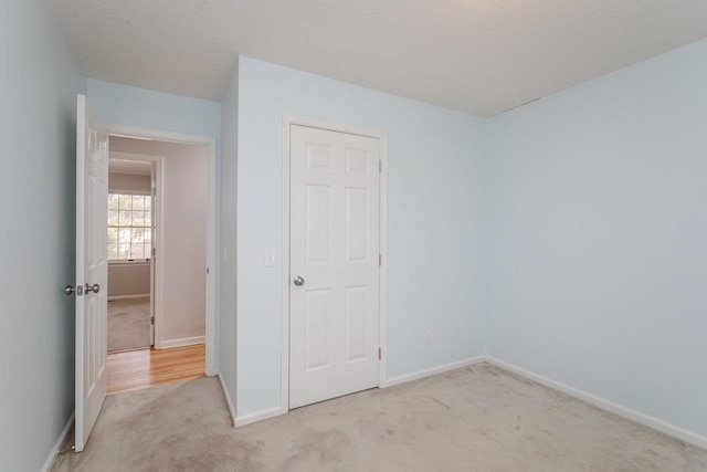 unfurnished bedroom with light colored carpet, a textured ceiling, and baseboards