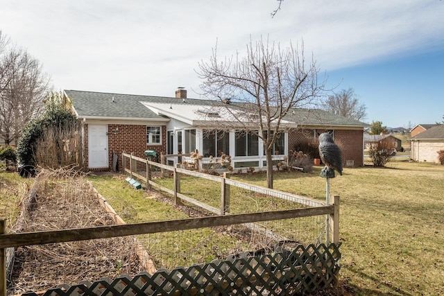 rear view of property featuring fence, a yard, a shingled roof, brick siding, and a chimney