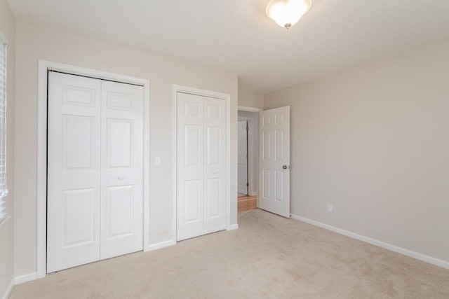 unfurnished bedroom featuring carpet flooring, baseboards, multiple closets, and a textured ceiling