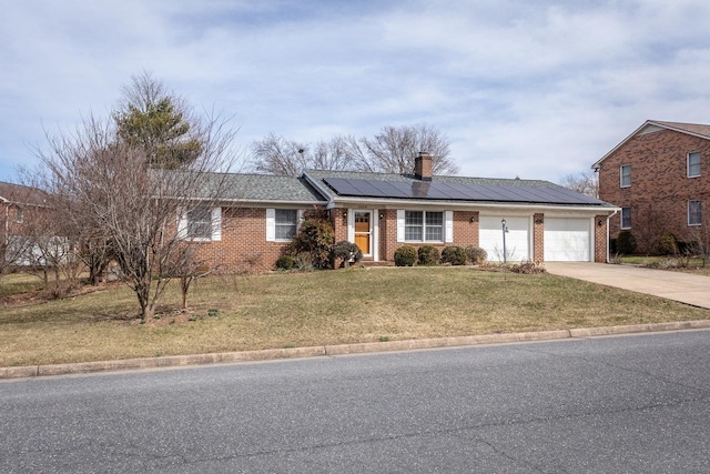 ranch-style home with a front lawn, driveway, roof mounted solar panels, a garage, and brick siding