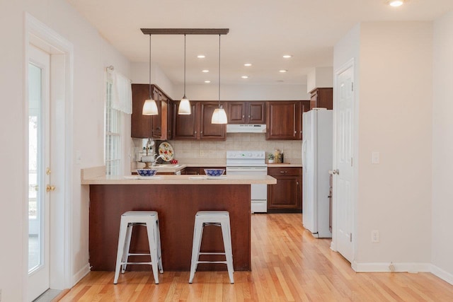 kitchen with under cabinet range hood, tasteful backsplash, white appliances, light wood-style floors, and light countertops