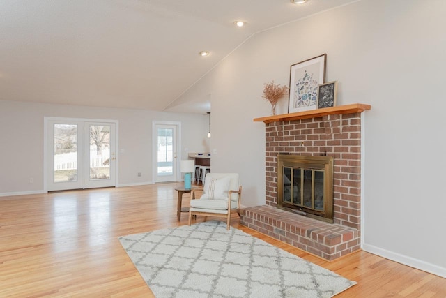 living area with a brick fireplace, baseboards, lofted ceiling, and wood finished floors