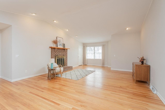 living area featuring baseboards, light wood finished floors, a brick fireplace, and vaulted ceiling