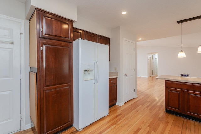 kitchen featuring light wood finished floors, recessed lighting, hanging light fixtures, light countertops, and white fridge with ice dispenser