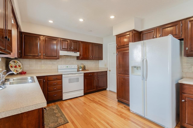 kitchen with white appliances, a sink, light wood-style floors, under cabinet range hood, and tasteful backsplash