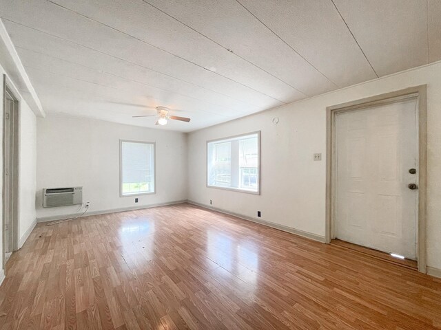 unfurnished living room featuring ceiling fan, a wall unit AC, and light hardwood / wood-style flooring