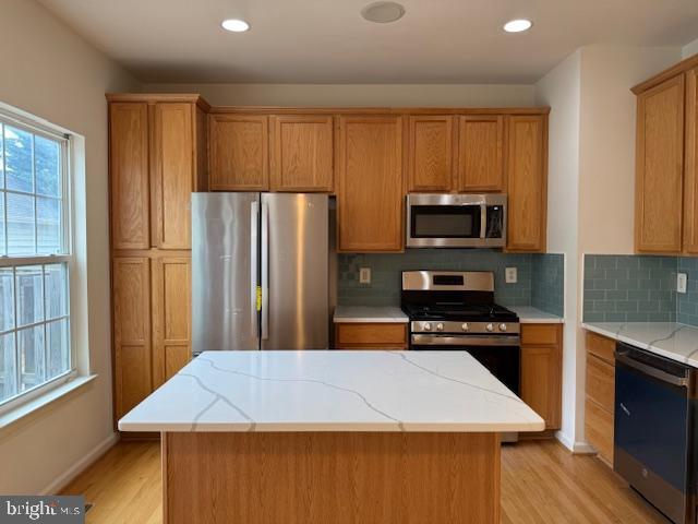 kitchen featuring backsplash, a center island, light stone countertops, light wood-type flooring, and appliances with stainless steel finishes