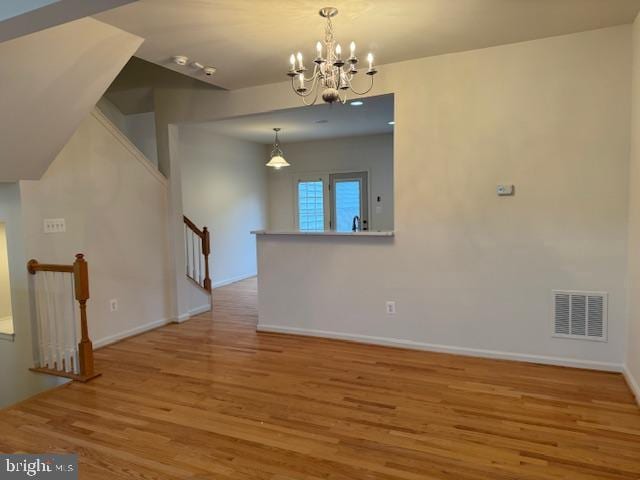 unfurnished room with baseboards, wood finished floors, visible vents, and a chandelier