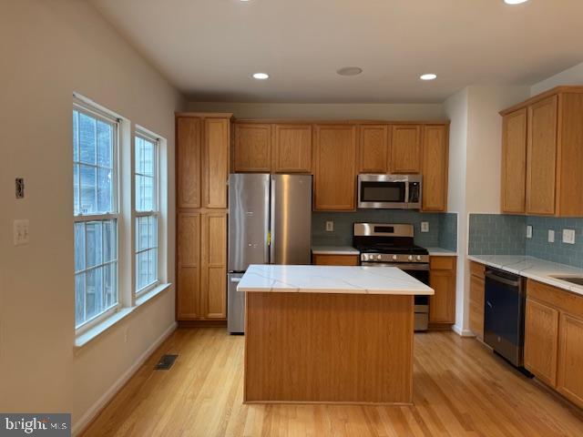 kitchen featuring a center island, tasteful backsplash, light wood finished floors, and stainless steel appliances