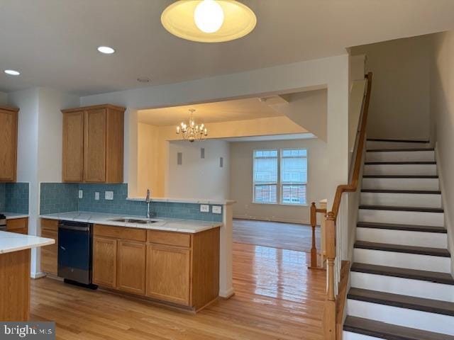 kitchen with a sink, light wood finished floors, decorative backsplash, dishwasher, and light countertops