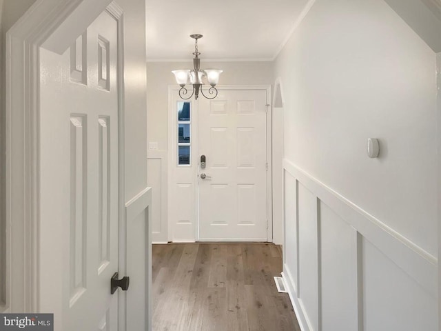 doorway to outside with crown molding, an inviting chandelier, and light hardwood / wood-style flooring