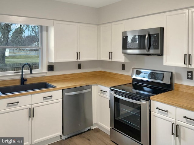 kitchen featuring sink, wooden counters, stainless steel appliances, white cabinets, and hardwood / wood-style flooring