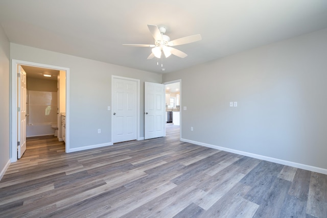 unfurnished bedroom with connected bathroom, baseboards, and wood finished floors