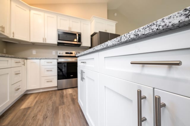 kitchen with white cabinets, light stone counters, stainless steel appliances, wood finished floors, and lofted ceiling