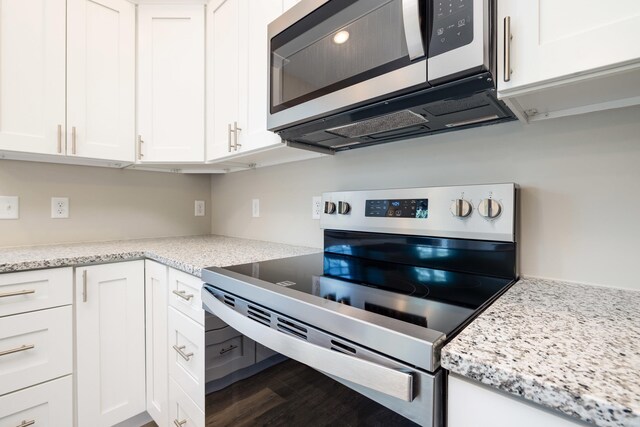 kitchen with light stone counters, white cabinets, stainless steel appliances, and wood finished floors