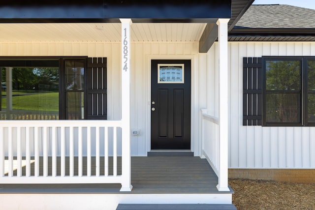 entrance to property featuring covered porch and roof with shingles