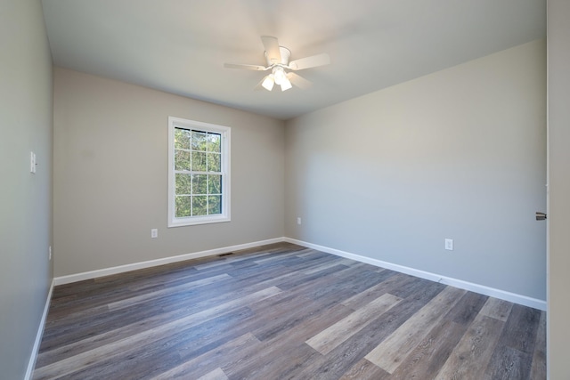 empty room featuring dark wood-style flooring, a ceiling fan, and baseboards