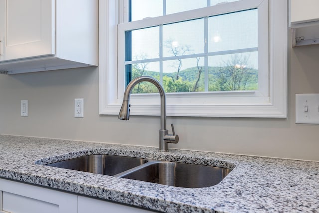 interior details featuring light stone counters, a sink, and white cabinets