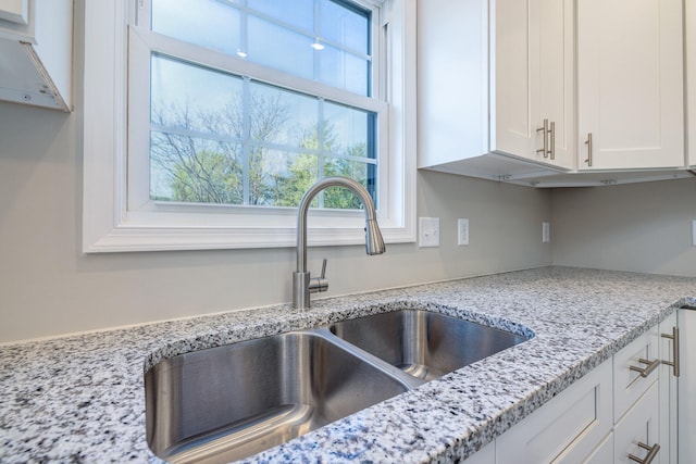 kitchen with light stone counters, a sink, and white cabinets