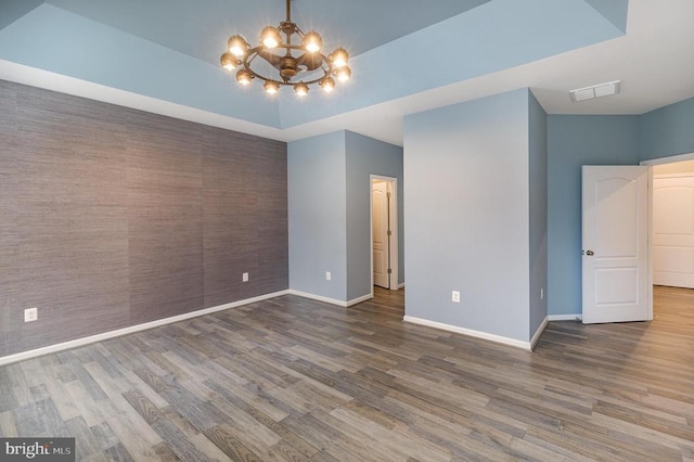 empty room featuring wood finished floors, baseboards, visible vents, a raised ceiling, and a notable chandelier