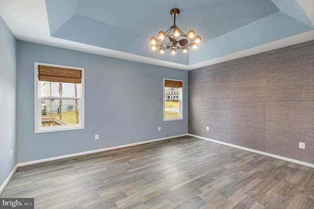 empty room featuring a raised ceiling, plenty of natural light, baseboards, and a chandelier