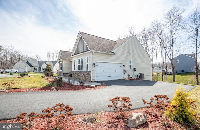 view of side of home with board and batten siding, central AC, a garage, stone siding, and driveway